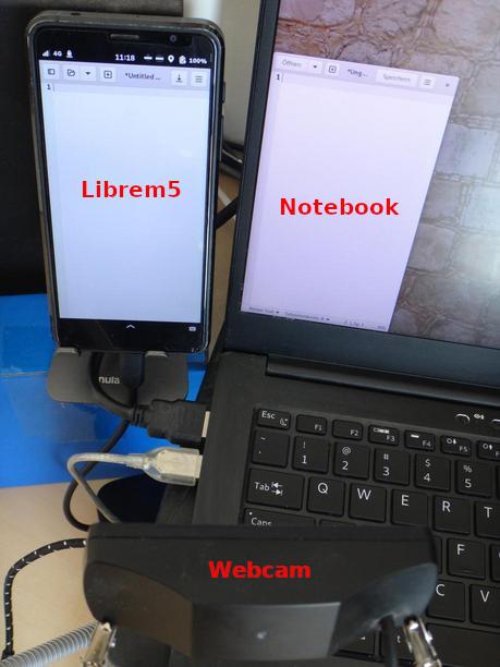 A picture showing a webcam in front of a Librem5 on the left and part of a notebook screen to the right. 'Librem5', 'notebook' and 'webcam' is written on the picture over the placing of the devices.