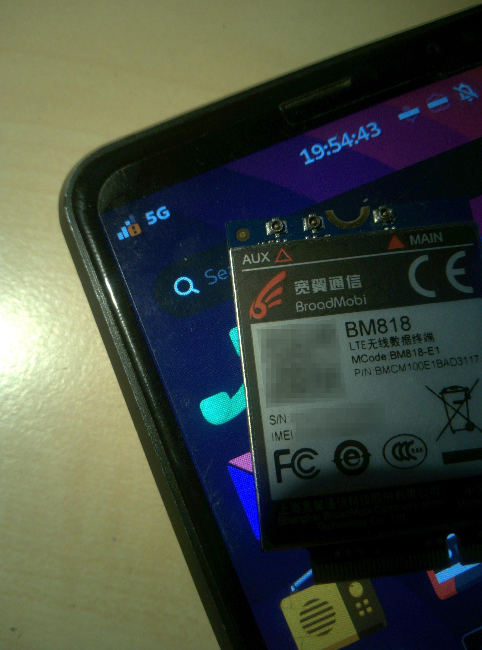 Picture of a #Librem5 front upper left corner with scren on showing a 5G icon beside the signal strength indicator. On the screen there's a m2 modem module BM818 lying.