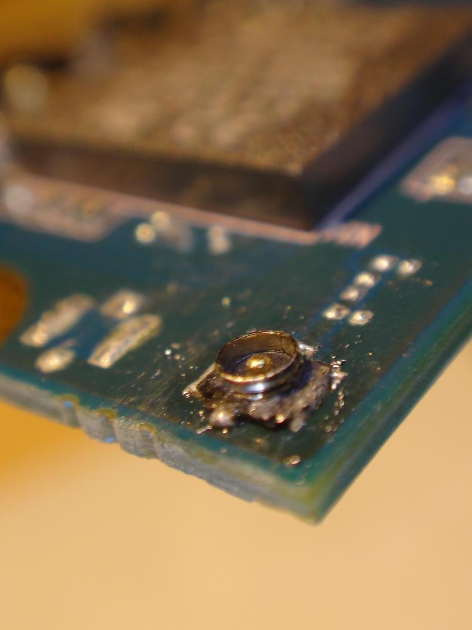 2nd try: Macro picture of a antenna cable socket on the corner of a green pcb. Soldering looks like it could hold the socket to the pcb, but still messy…