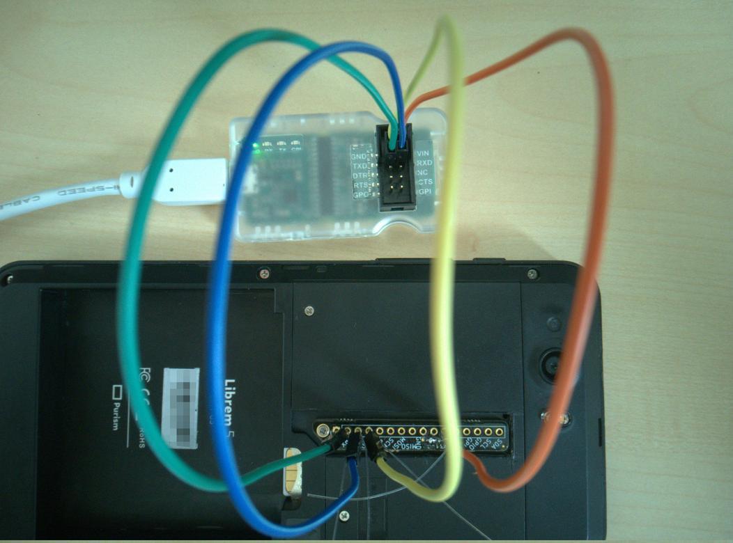 Backside of an open Librem5 with a breakout board installed. Cables running from the serial pins and 3.3V to a μArt serial-usb adapter connected to a white usb-cable.