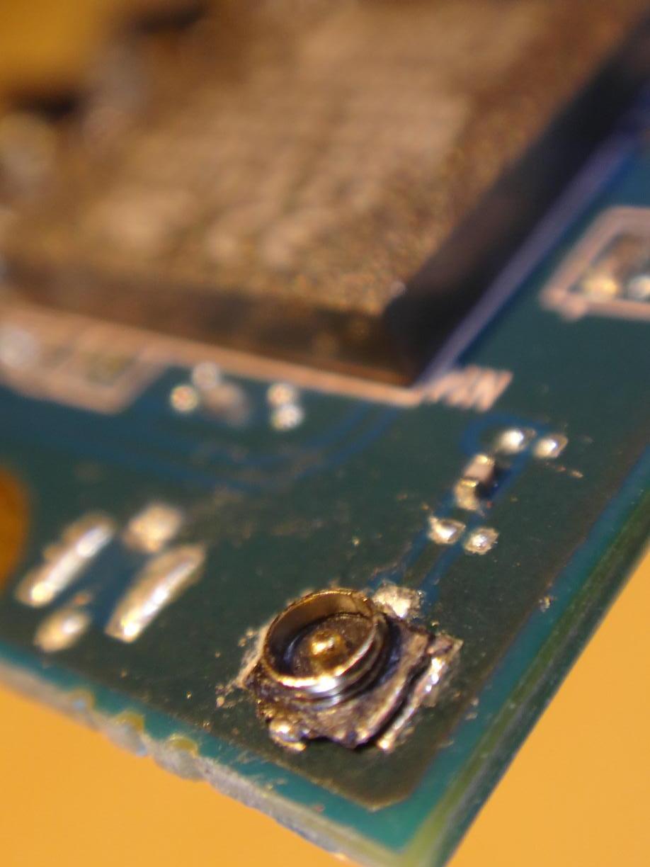 1st try: Macro picture of a tiny smd antenna cable socket on the corner of a green pcb. Soldering does not look like inspiring much confidence…